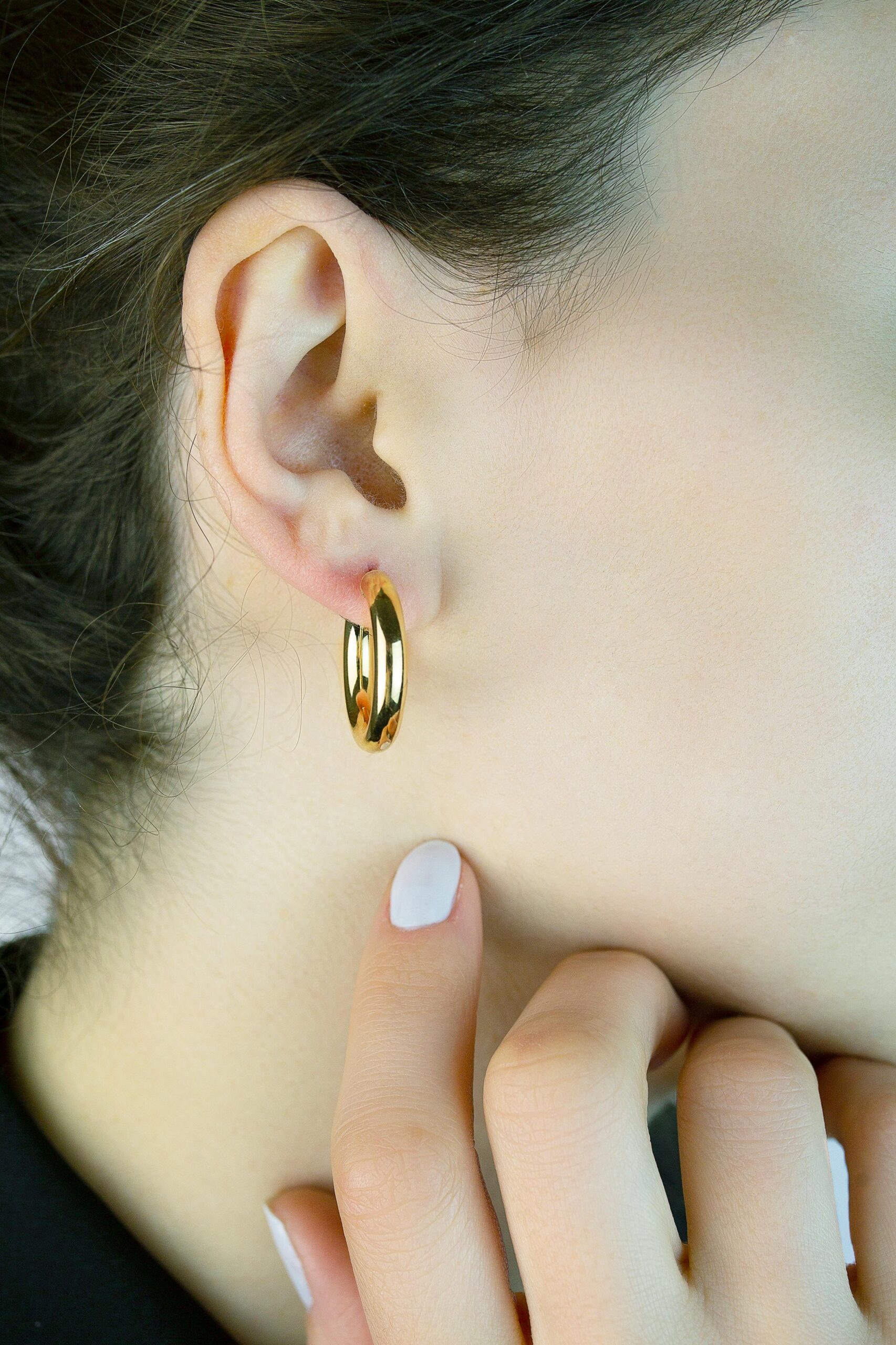 Close-up of a woman's ear adorned with a luxurious gold earring, highlighting skin texture.